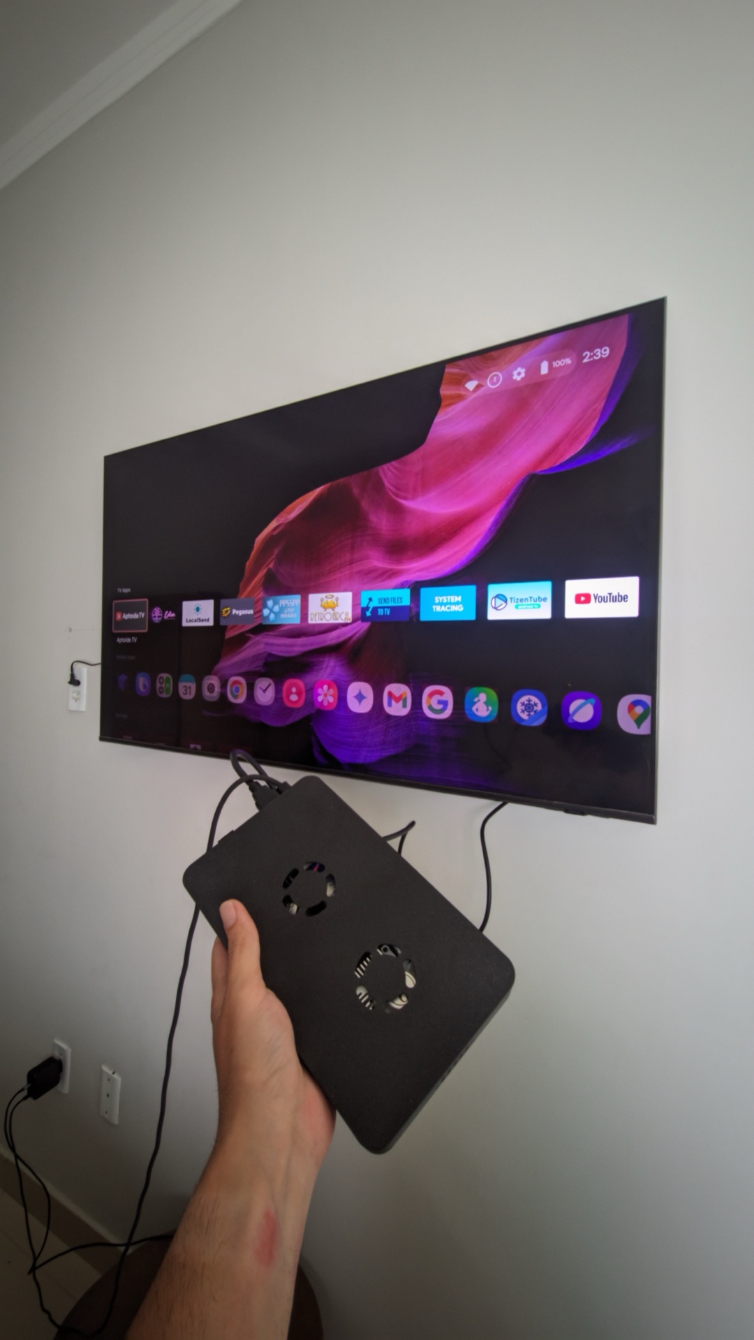 O Galaxy Z Flip 5 transformado em TV Box — a case preta com coolers na mão, ligada à TV mostrando o launcher Android.